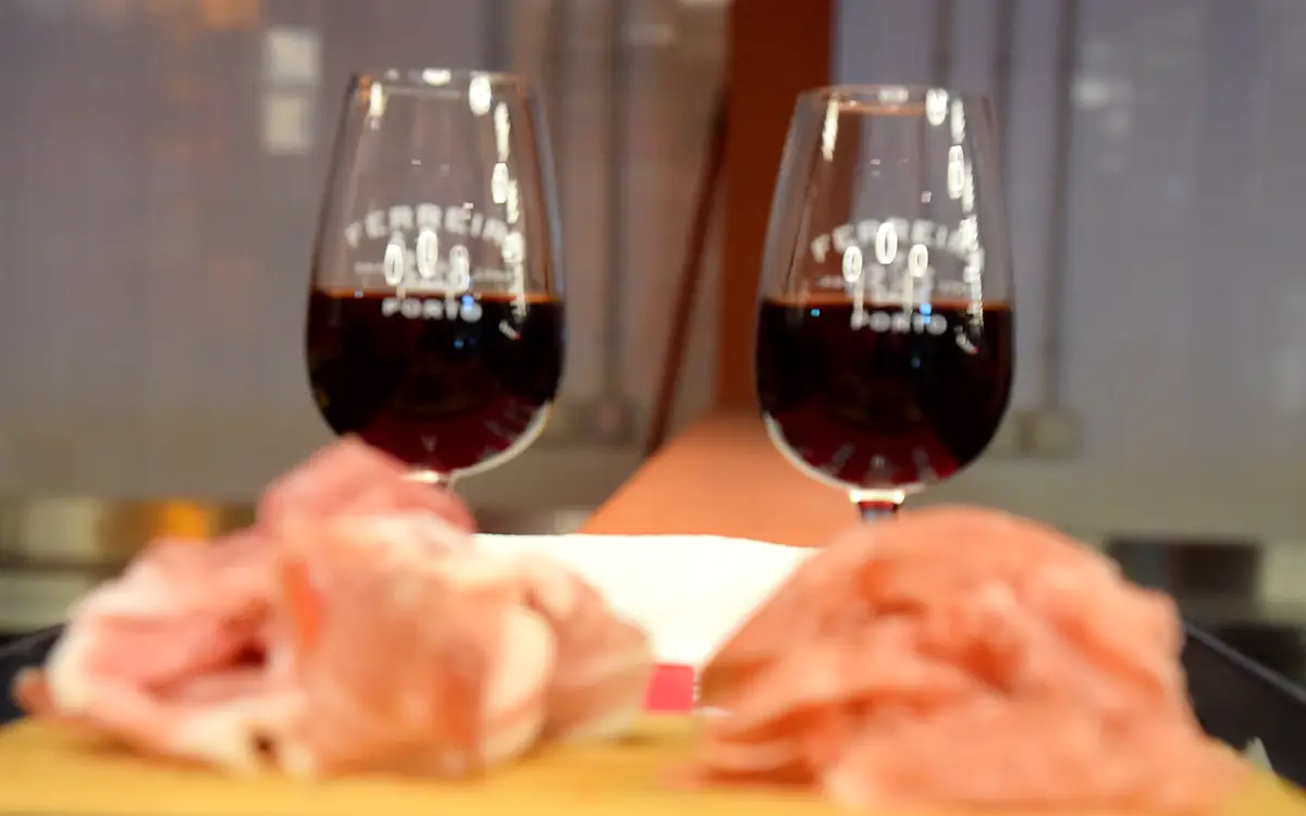 Twee glazen rode port met plakjes ham op een houten plank