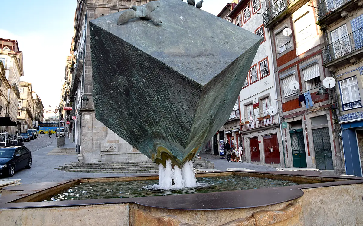 De bronzen kubussculptuur op de Praça da Ribeira, staand boven het water van de fontein, met de gevels van het plein eromheen