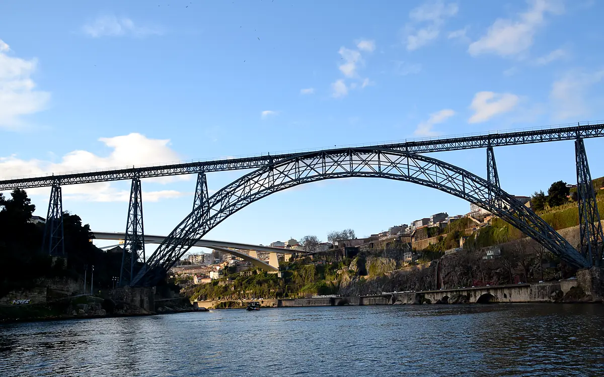 De ijzeren boog van de Ponte Maria Pia met daarachter de witte betonnen Ponte de São João, gezien vanaf het water