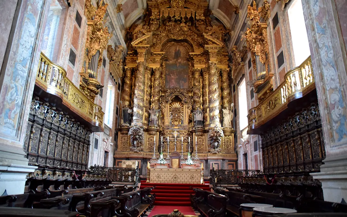 Het vergulde hoofdaltaar van de kathedraal van Porto met het houten koorgestoelte ervoor en een rode loper naar de treden