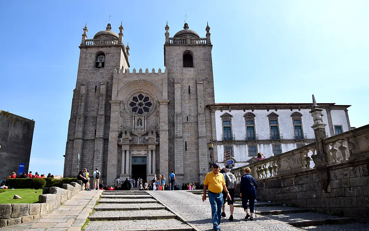 De voorgevel van de kathedraal van Porto met het rozetvenster tussen twee torens, met de trap ervoor en het bisschoppelijk paleis ernaast
